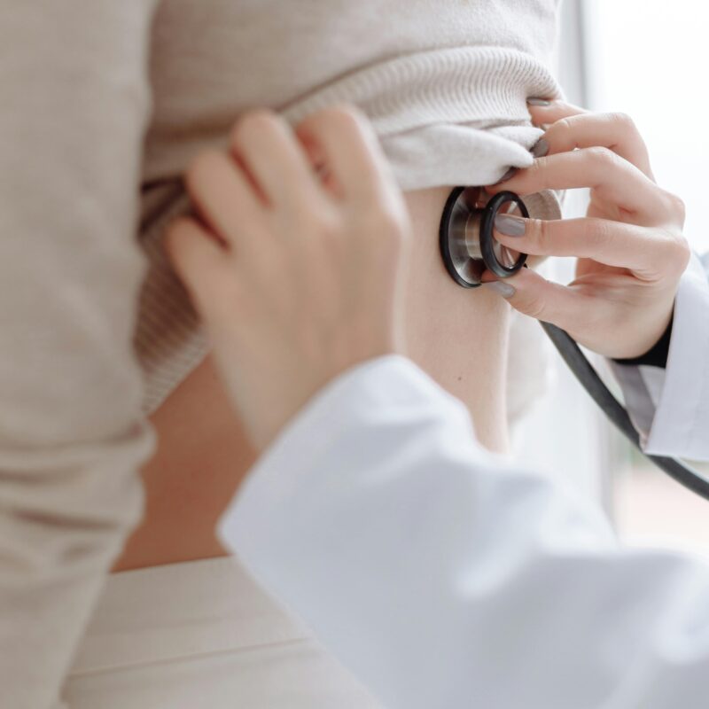 Doctor listening to patient's heartbeat or breathing from the back during a women's health exam
