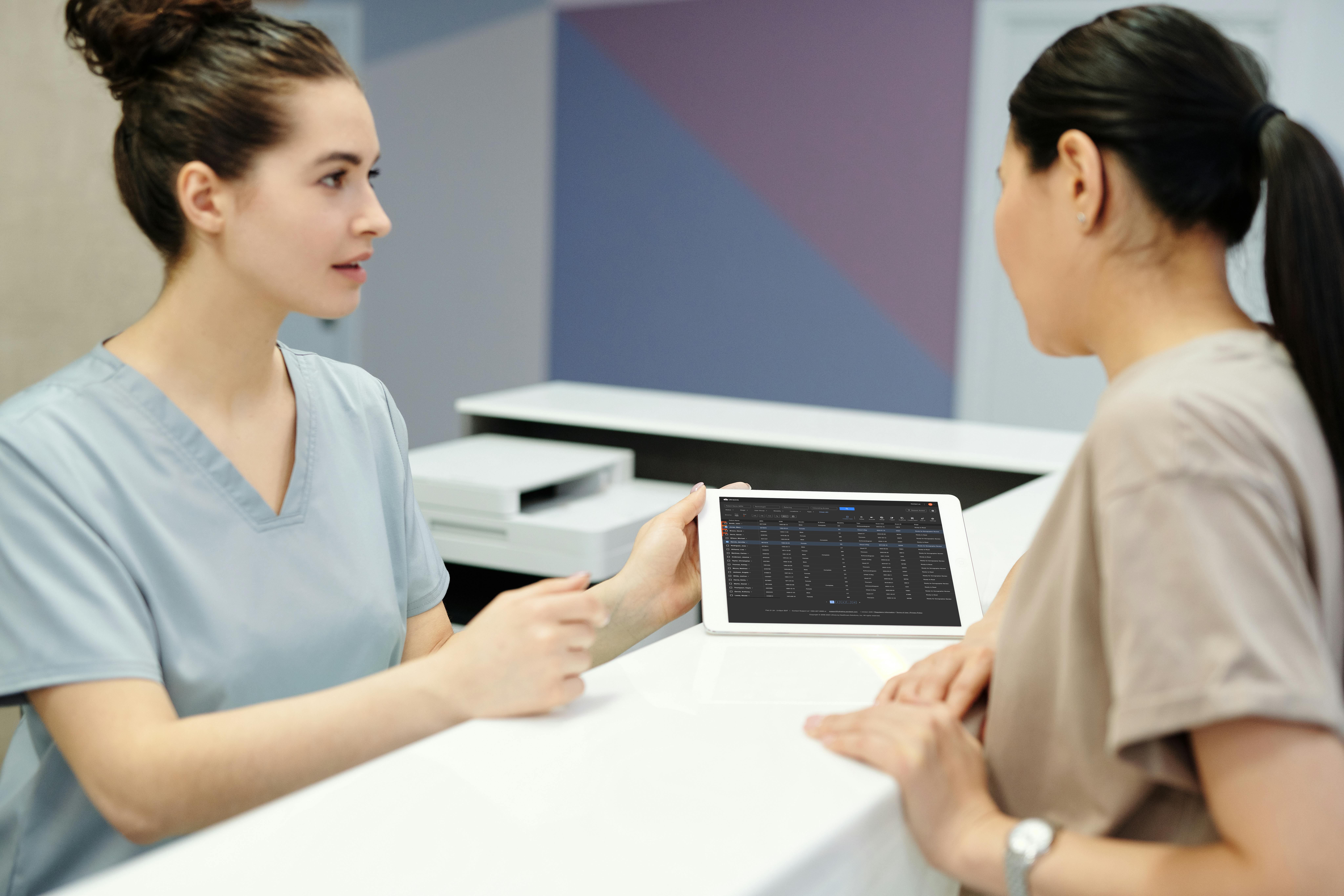 Two female healthcare professionals discussing a medical imaging dashboard displayed on a tablet, featuring UltraLinQ's cloud-based PACS system in dark mode.